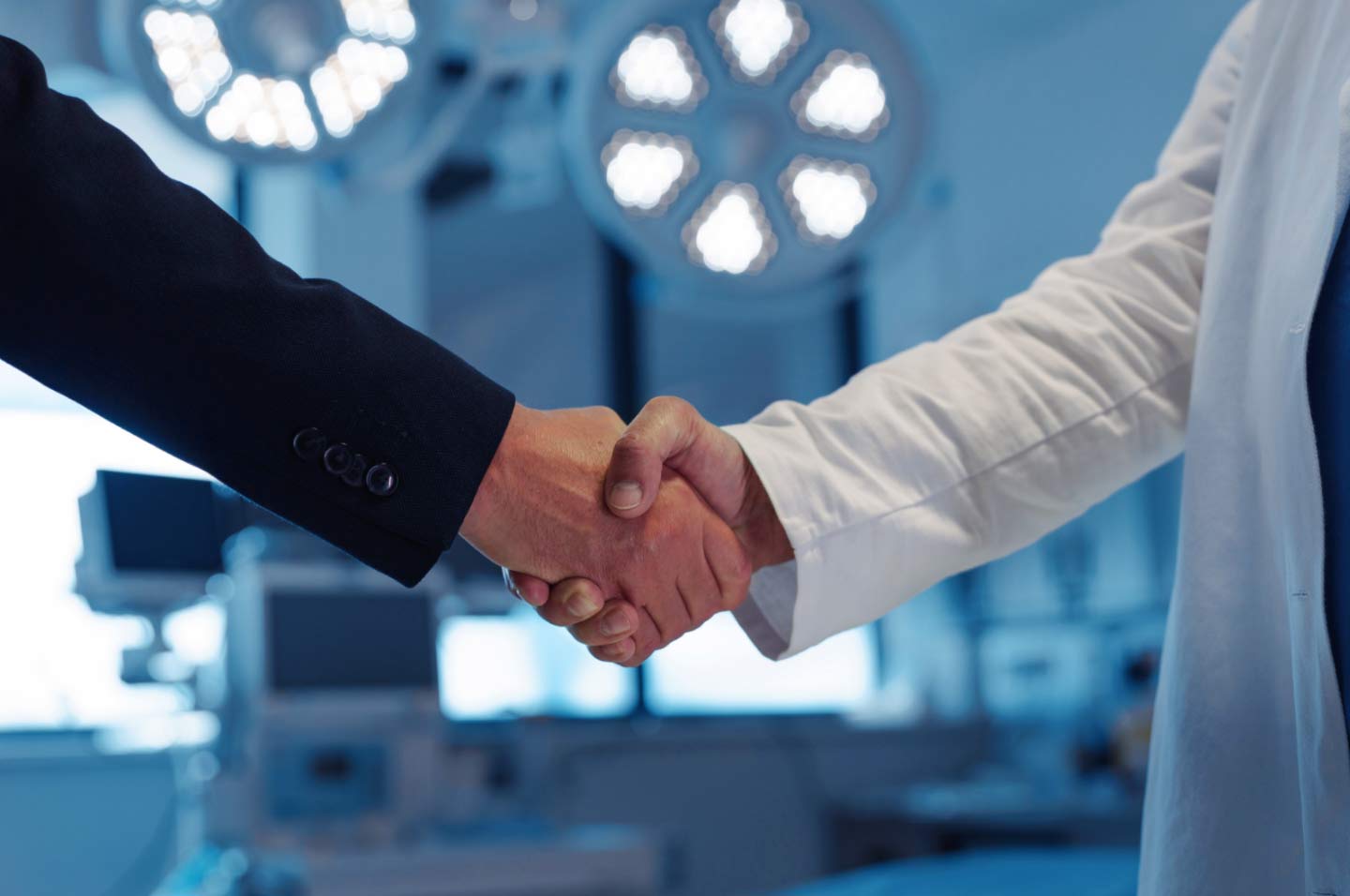 A doctor and a person in a suit shaking hands in a brightly lit medical setting.