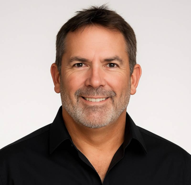 Smiling middle-aged man with short brown hair and beard, wearing a black collared shirt on a white background.